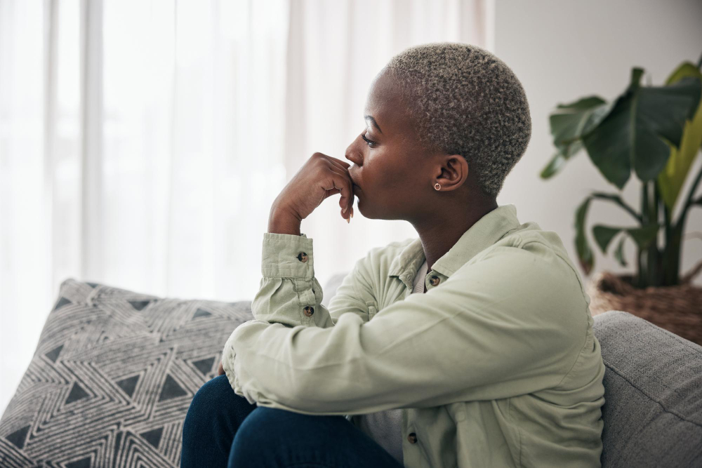 Woman thinking and depression on sofa for sad memory mental health risk and anxiety of debt stress worry and lonely african person remember trauma of abuse broken heart or doubt decision at home