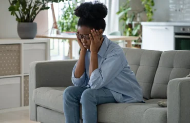 Discouraged sad african american woman sits on sofa and feeling stressed because of loneliness