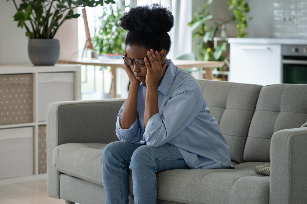 Discouraged sad african american woman sits on sofa and feeling stressed because of loneliness