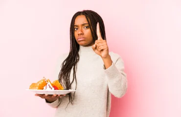 Young african american woman holding a waffle isolated showing number one with finger