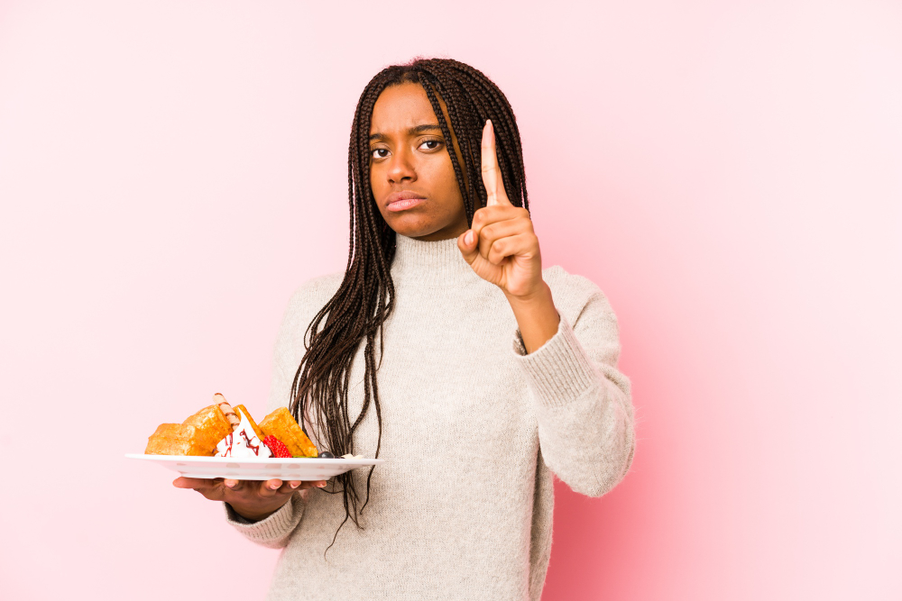 Young african american woman holding a waffle isolated showing number one with finger