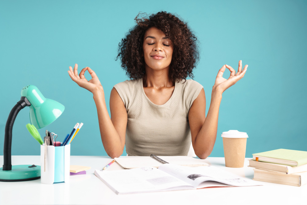 Beautiful smiling young african businesswoman casually dressed sitting at the desk isolated over blue wall, meditating while studying