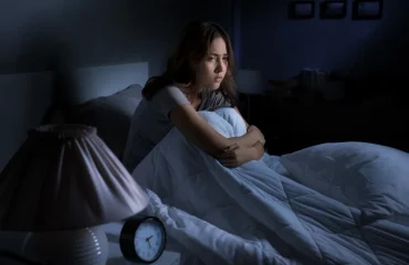 Depressed young woman sitting in bed cannot sleep from insomnia