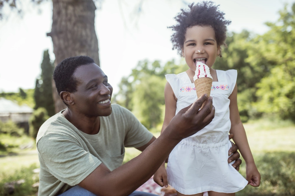 Sweet tooth. Dark-skinned cute kid eating ice-cream and spending time with dad