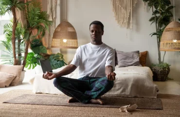 Young African man meditating sitting at his bedroom in the morning alone