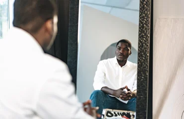 african man Bipolar Disorder sitting against mirror indoors