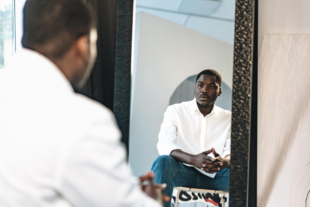 african man Bipolar Disorder sitting against mirror indoors