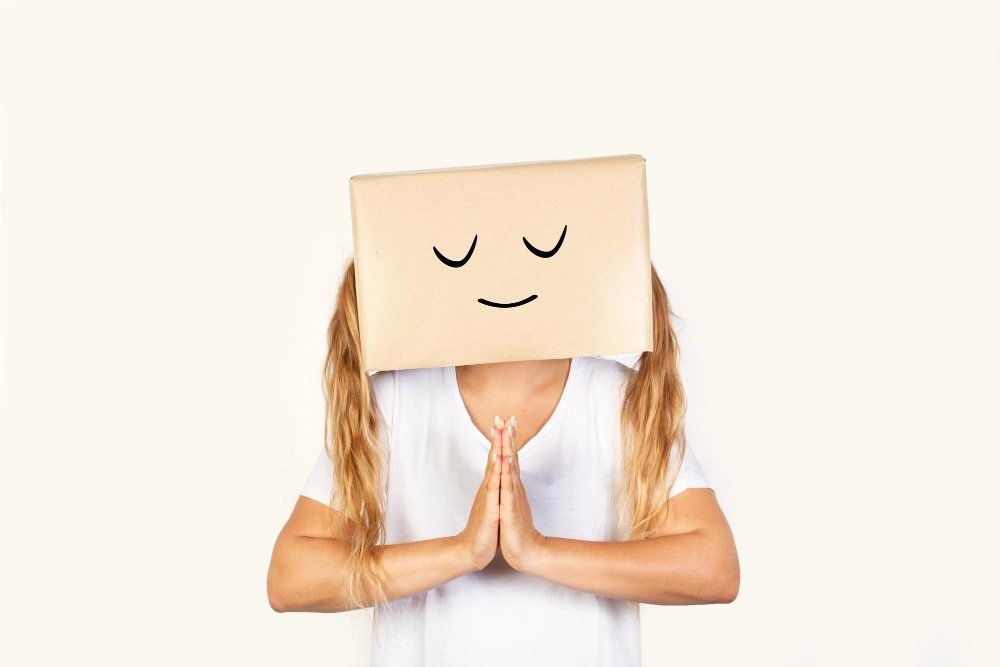 Woman with her head in a box and praying gesture standing on a white background with copy space