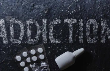 The concept of drug dependence, pills, nasal spray. Black background with white inscription addiction and medicines